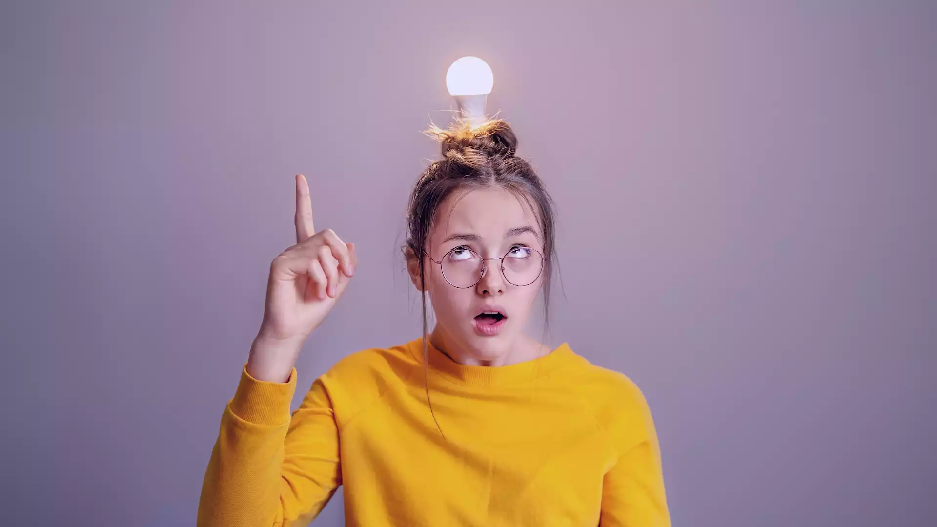 A girl is being filmed in a studio with a light bulb on her head, representing ideas relating to setting up a video studio as well as different projects that can be filmed in a video studio.