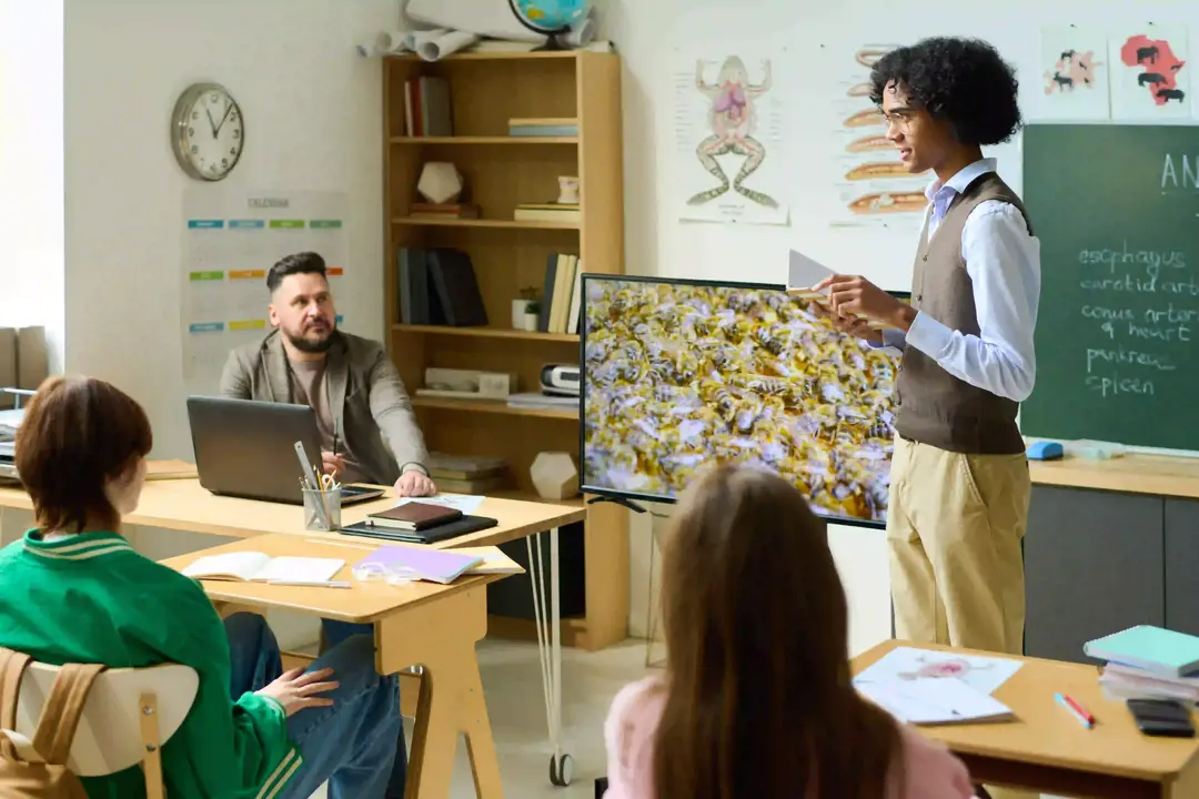 Someone is standing in a classroom with a screen next to him. This represents moving away from traditional video hosting to Cinema8 for more flexibility.